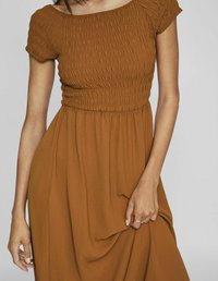 Rochie maro, cu pliuri, cu mâneci scurte, decolteu în formă de U și fustă fluidă. Fabricată dintr-un material texturat, care pune în evidență drapajul delicat.