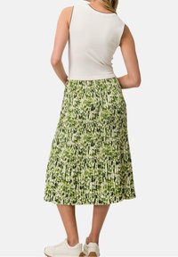 Weißes ärmelloses Oberteil kombiniert mit einem grünen, plissierten Midirock mit Blattdruck, ergänzt durch weiße Sneaker.