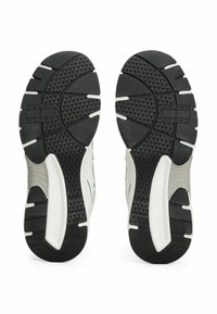 Soli di scarpe sportive bianche e nere caratterizzati da un motivo di battistrada testurizzato, con una pronunciata trazione in gomma e un logo impresso sul suolo sinistro.