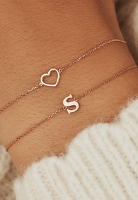 Roze gouden armband met een hart- en letter "S" bedel, delicate kettingontwerp, gladde textuur en dunne schakel. Draagt om een pols.