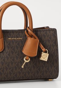 Sac à main brun avec motifs, accents en cuir beige, quincaillerie dorée, détail de clé et de cadenas, présentant un design structuré et des poignées doubles.