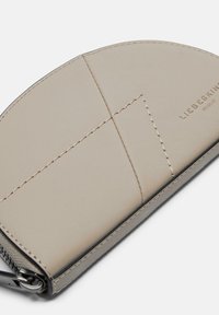 Cartera de cuero en beige claro, con detalles de costura, una textura suave y una forma elegante. Marca visible en la superficie.