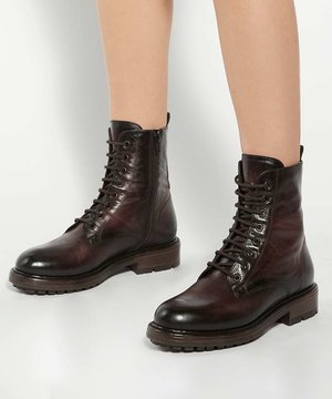 Bottines en cuir marron foncé à lacets avec fermetures éclair latérales portées sur des jambes nues sur fond blanc.