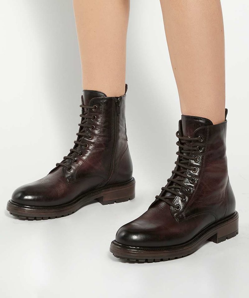 Bottines en cuir marron foncé à lacets avec fermetures éclair latérales portées sur des jambes nues sur fond blanc.