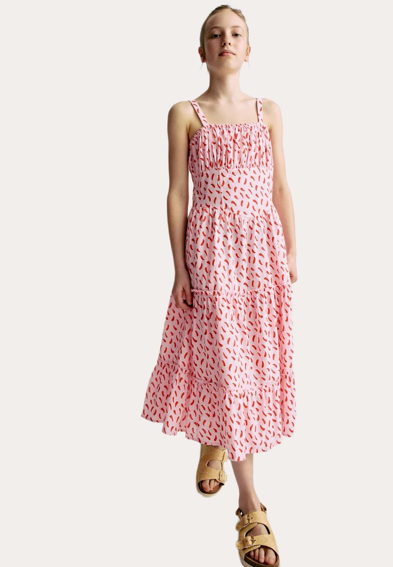 Rosa ärmlös maxiklänning med röda abstrakta mönster, elastisk midja, lager-på-lager kjol, och ihop med beige sandaler. Enkel design, lättviktsmaterial.