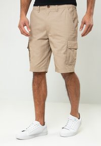 Shorts cargo kaki en tissu mélangé coton ; dotés de plusieurs poches latérales et de détails cousus ; portés avec des baskets blanches.