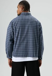 Blauw-zwart geblokt flanellen overhemd met lange mouwen en een losse pasvorm; voorzien van een kraag en geruite manchetten met knopen.