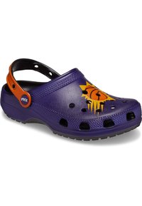 Fioletowe Crocs z logo słońca koszykarskiego, czarne perforacje zapewniające wentylację oraz regulowany pomarańczowy pasek na pięcie. Teksturowana powierzchnia.