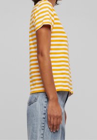 Striped t-shirt featuring yellow and white stripes, short sleeves, a relaxed fit, and a round neckline, paired with light blue jeans.