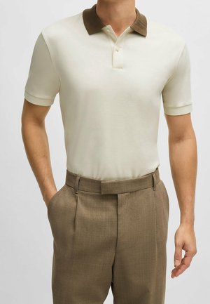 Polo en écru avec un col marron, des manches courtes et une patte de boutonnage à trois boutons, associé à un pantalon marron ajusté.