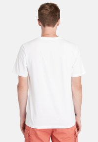 Baltas trumpas rankovėmis T-shirt, pagamintas iš medvilnės, suapvalintu kaklu. Lygus audinys, laisvas kirpimas ir mažas ženkliukas kairiajame apatiniajame kampe.