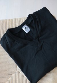Sort v-hals t-shirt lavet af 100% bomuld, ligger fladt, har et mærke med størrelse og materialeinformation nær halsudskæringen.