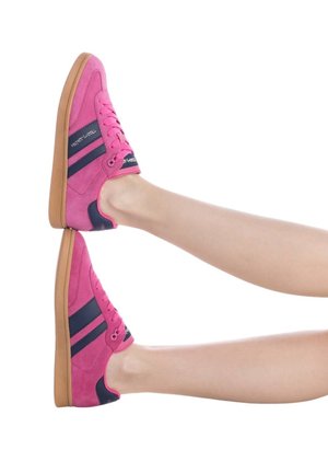 Scarpe da ginnastica in suede rosa con strisce blu navy, design con lacci e suole in gomma beige, viste di lato con le gambe distese.