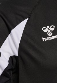 Sort-hvidt sportstrøjestof med et hvidt Hummel-logo med en stiliseret bi på brystområdet.
