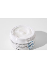 Crème enrichie en puissance d'hydratation dans un contenant rond blanc, avec une texture lisse et épaisse et un couvercle à vis, comportant un texte bleu et noir.