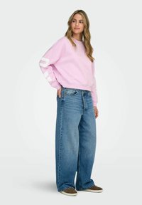 Hele roosa dressipluus valgete graafiliste elementidega varrukaid, kombineeritud suurte siniste teksade ja pruunide tossudega. Vabaaja tänavastiil.