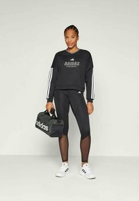 Sweatshirt preto cropped com o logótipo branco da Adidas, leggings pretas e ténis brancos. Mala de treino preta com detalhes brancos no logótipo.
