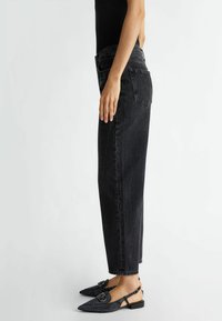 Jeans negros de tiro alto con corte recto, que presentan una sutil textura y cinco bolsillos, combinados con zapatos planos negros tipo slingback decorados con una hebilla.