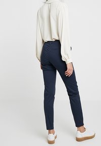 Granatowe slim-fit spodnie wykonane z tkaniny tkanej, w połączeniu z kremową bluzką. Strój charakteryzuje się gładką teksturą, a spodnie mają czystą sylwetkę.