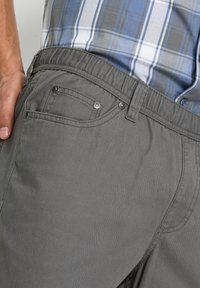 Pantaloni corti grigi realizzati in tessuto leggero, caratterizzati da una texture liscia, passanti per la cintura, due tasche frontali e dettagli decorativi in metallo.