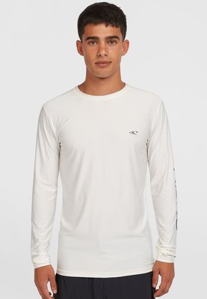 Long-sleeve, cream-colored shirt made of a lightweight, stretchy material. Features a small logo on the chest and text along the sleeve.