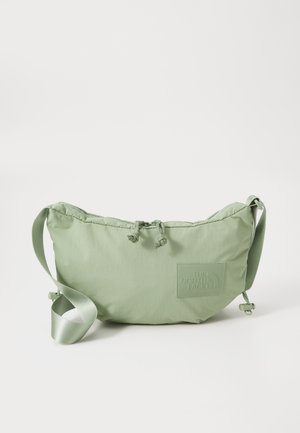 Bolsa de ombro puffy em verde claro, feita de um tecido macio, apresentando um patch de logotipo texturizado, fecho de cordão e uma alça de cetim.