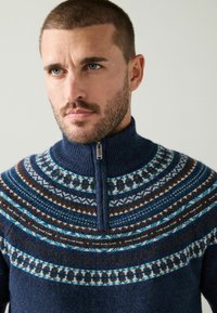 Marineblauer Pullover mit Reißverschluss und hohem Kragen, mit einem gemusterten Einsatz in Blau-, Braun- und Weißtönen. Hergestellt aus weicher Wollmischung.