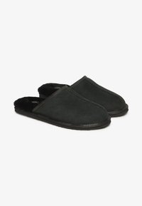 Zapatillas de ante negro con un suave forro de piel negra, diseño de punta redonda y suela de goma plana. Acentos de costura simples en la parte superior.