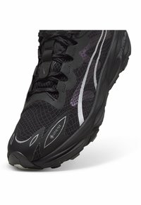 Zwarte hardloopschoen met een gestructureerde synthetische bovenkant, reflecterende accenten, Gore-Tex labeling en een duurzame rubberen zool.
