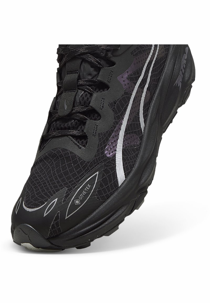 Chaussure de running noire avec une tige synthétique texturée, des accents réfléchissants, une étiquette Gore-Tex et une semelle en caoutchouc durable.