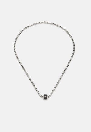 Collier en chaîne argentée avec un petit accent cubique noir portant un logo au centre. La chaîne présente une texture lisse et des maillons géométriques.