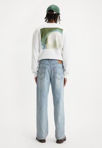Witte sweatshirt met een grote grafische print van een planeet op de achterkant, gecombineerd met lichtblauwe losse jeans en bruine schoenen.