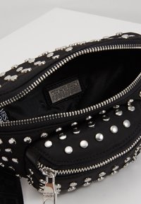 Borsa in tessuto nero con borchie argentate, chiusura con zip e un interno liscio. Presenta un'etichetta con logo all'interno, che offre un design texturizzato.