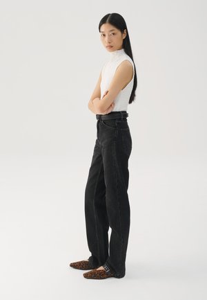 Schwarze weite Jeans mit hoher Taille, kombiniert mit einem strukturierten, weißen ärmellosen Oberteil und braunen Flats im Leopardenmuster. Schlichte, moderne Styling.