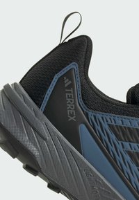 Czarny but sportowy z teksturowaną siateczką, niebieskimi akcentami, gumową podeszwą i widocznym logo. Posiada pętelkę na pięcie ułatwiającą zakładanie.