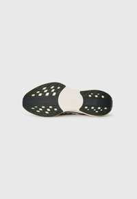 Semelle d'une chaussure de course Nike noire et blanche avec une texture antidérapante et un logo sur le dessous, présentée sur un fond blanc.