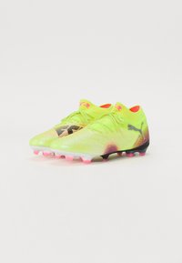 Botas de fútbol amarillas brillantes con un diseño texturizado, acentos en negro y rosa, un collar ajustado y múltiples tacos rosas en la suela.