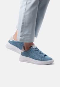 Blå lädersneakers med perforerat mönster, vit sula, ljusgrå detaljer och blå snören, matchade med ljustvättade denimbyxor.