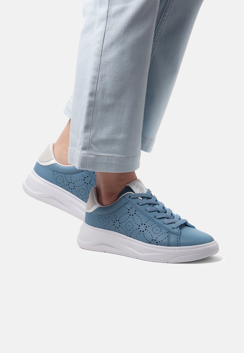 Blå lädersneakers med perforerat mönster, vit sula, ljusgrå detaljer och blå snören, matchade med ljustvättade denimbyxor.