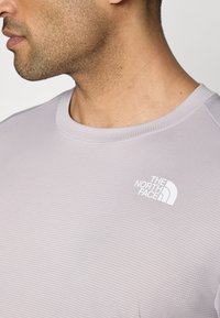 Soehall hall, lühikeste varrukatega heledates toonides särk, millel on tekstuuriga disain ja ümar krae. Rinnal on valge "The North Face" logo.