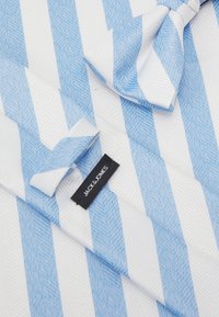 Corbata tejida en azul y blanco con patrones de rayas alternas en una textura de espiga, que presenta una etiqueta de la marca "JACK & JONES" en negro.