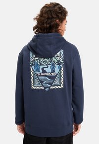 Sudadera azul marino con un gran gráfico colorido en la parte posterior que presenta montañas, cactus y patrones geométricos. Textura de tela suave.