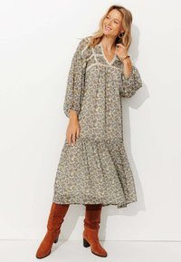 Robes maxi à motif floral en tissu léger, avec un décolleté en V, des manches longues et une jupe à volants. Associée à des bottes jusqu'aux genoux orange-brun.