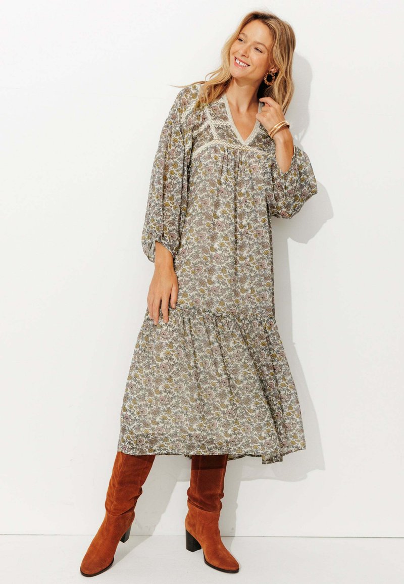 Robes maxi à motif floral en tissu léger, avec un décolleté en V, des manches longues et une jupe à volants. Associée à des bottes jusqu'aux genoux orange-brun.