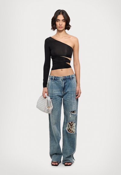 Black one-shoulder top with cut-out detailing, paired with light blue distressed wide-leg jeans and a textured silver handbag.