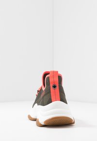 Vihreät verkkokengät, joissa on rakenteellinen takaosa, oranssit yksityiskohdat ja teksturoitu valkoinen välipohja. Kengissä on musta logo kantapäässä ja nauhakiinnitys.