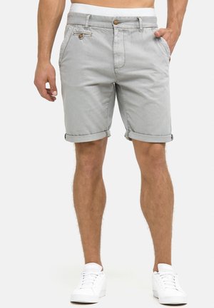 Light gray cotton shorts with rolled hem, front pockets, and wooden button detail. Paired with white sneakers. Smooth texture.