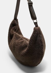 Hnedá štruktúrovaná taška cez rameno vyrobená z plyšového, mäkkého materiálu. Má zakrivený tvar a tmavý popruh s nastaviteľným kovovým prvkom.
