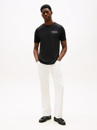 Black short-sleeve t-shirt with "HILFIGER" logo, paired with white wide-leg pants and black shoes. Smooth fabric, relaxed fit.