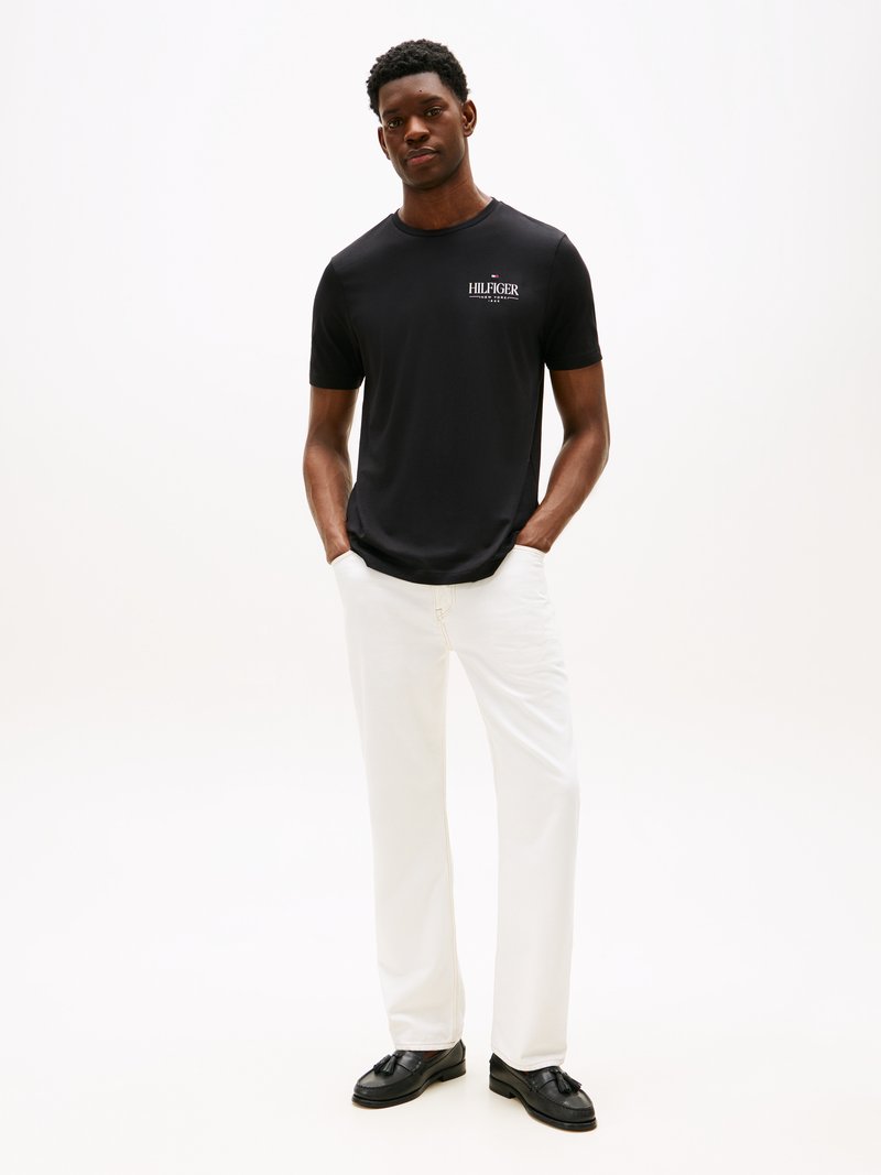 Black short-sleeve t-shirt with "HILFIGER" logo, paired with white wide-leg pants and black shoes. Smooth fabric, relaxed fit.